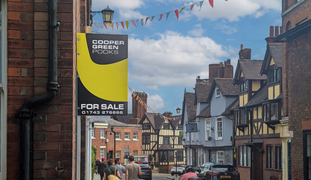 The Cooper Green Pooks Sales Board can be seen on the edge of a building. Taken on Dog Pole, Shrewsbury looks bright and beautiful in the background, with a blue sky and colourful bunting between the buildings.